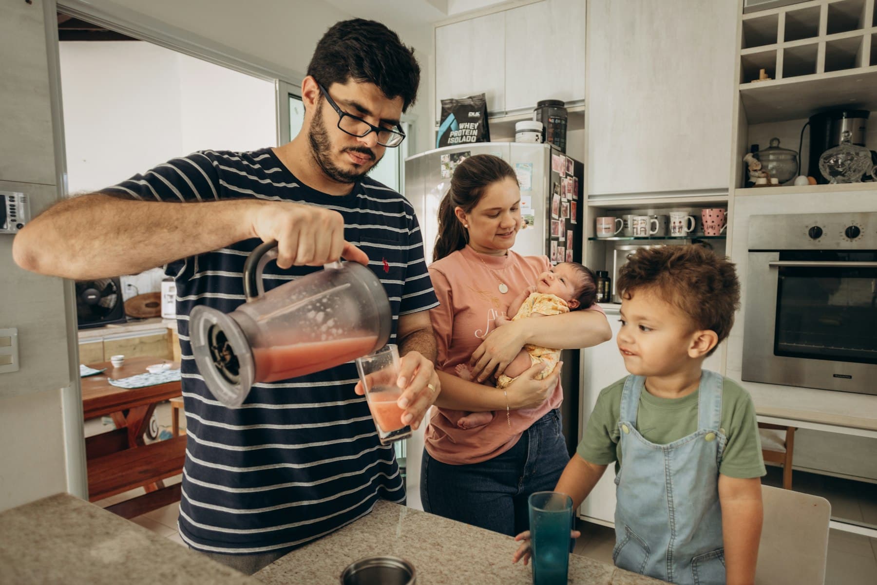 A man pours a drink for two children in a kitchen